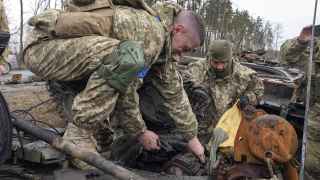 Украинские военные достают тело российского солдата из подбитого танка